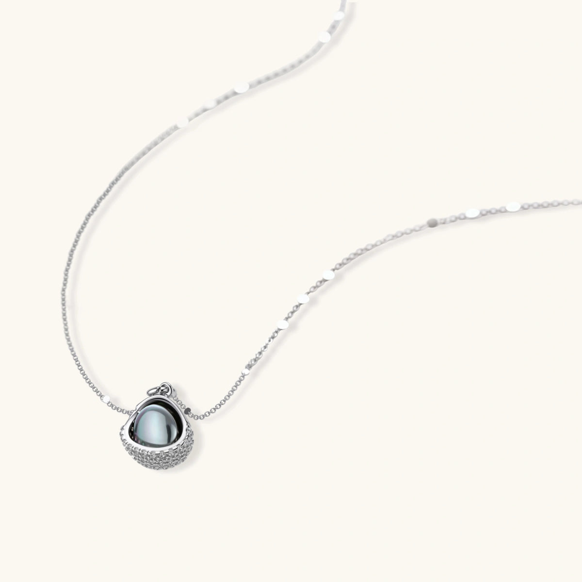 Silver gray Tahitian-style pearl pendant necklace and matching pave zirconia stud earrings set on cream background.